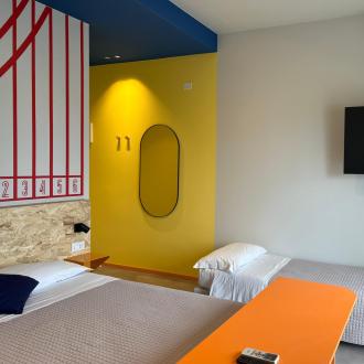 Buntes, modernes Zimmer mit Bett, TV und lebhaften Wänden.