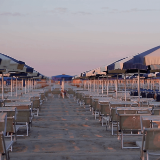 Spiaggia deserta con ombrelloni blu e lettini al tramonto.