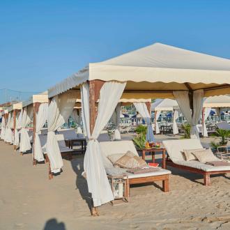 Gazebo sulla spiaggia con lettini e cuscini, atmosfera rilassante.