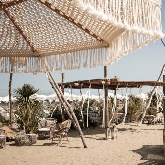 Spiaggia boho con sedie in vimini e ombrelloni decorati.