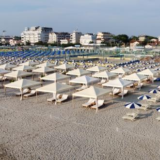 Spiaggia con ombrelloni e lettini, vista su edifici sullo sfondo.