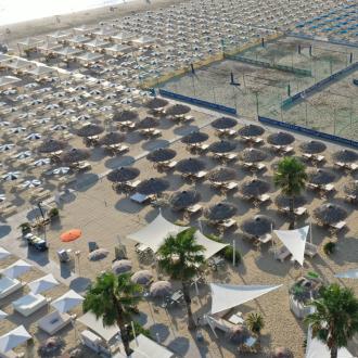 Spiaggia attrezzata con ombrelloni, lettini e campi sportivi.