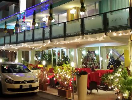 Hotel illuminato di notte con decorazioni natalizie e bandiere sulla facciata.