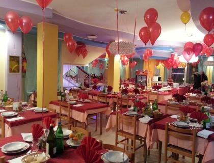 Ristorante decorato con palloncini rossi e tavoli apparecchiati per una festa.