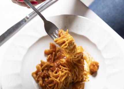 Nudeln mit Tomatensauce und Garnelen auf einem weißen Teller serviert.