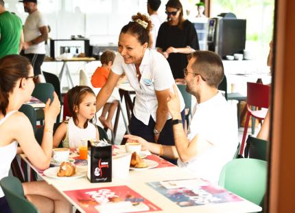 Familie beim Frühstück im Restaurant, bedient von einer lächelnden Kellnerin.