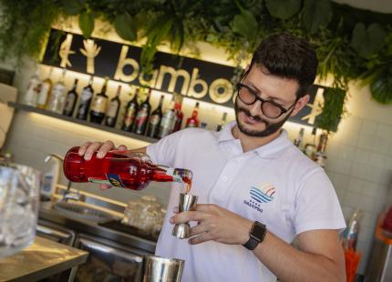 Barkeeper mixt Cocktail in einer Bar mit Pflanzen und Flaschen.