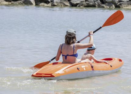 Zwei Personen im orangefarbenen Kajak auf ruhigem Wasser.