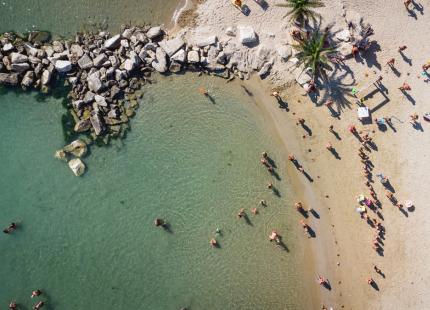 Überfüllter Strand mit orangefarbenen Sonnenschirmen, Luftaufnahme.