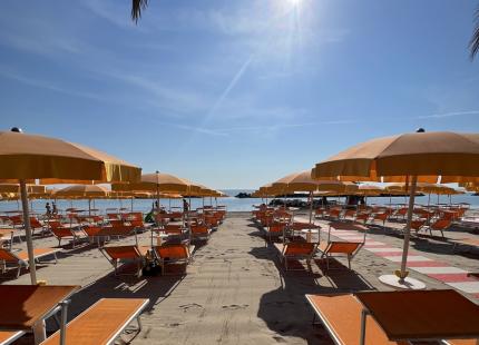 Strand mit orangefarbenen Sonnenschirmen unter der strahlenden Sonne.