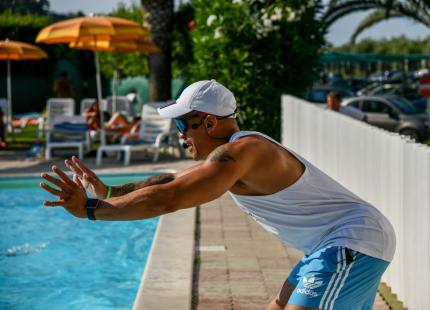 Mann am Pool dehnt sich mit weißer Kappe.