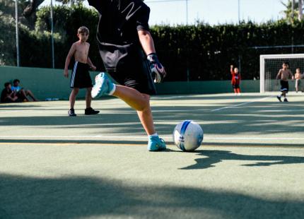 Kinder spielen Fußball auf einem Außenplatz.