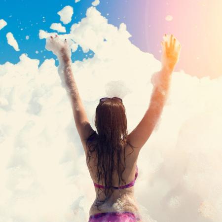 Person raises arms in foam under the sun.