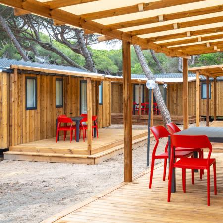 Outdoor area with red chairs and tables, wooden cabins.