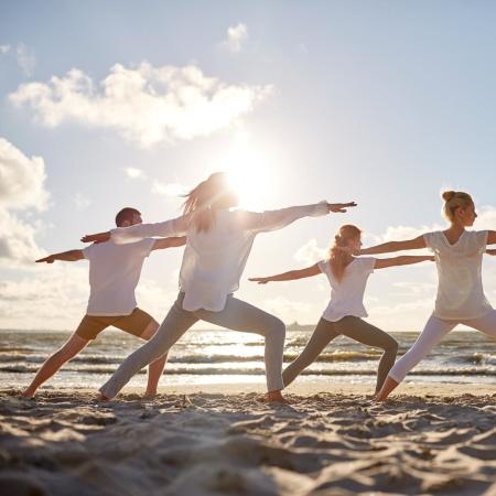 People doing yoga on the beach at sunset.
