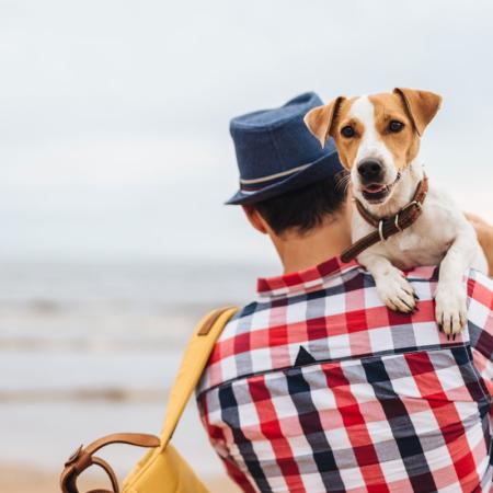 Man with dog on beach, wearing plaid shirt and hat.