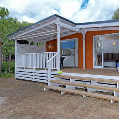 Wooden cabin with a porch and lounger, surrounded by nature.