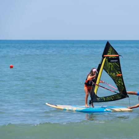 Child learns windsurfing with instructor in calm sea.