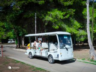 Electric shuttle with passengers in a nature-surrounded campsite.