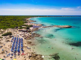 Plage bondée avec des parasols bleus et une eau cristalline.