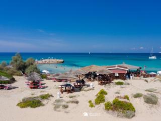 Plage avec parasols en paille, mer cristalline et bar sur le sable.