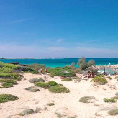 Spiaggia sabbiosa con mare turchese e chiosco.