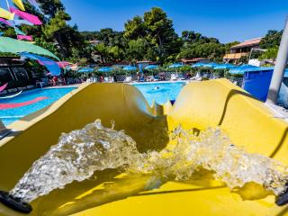 Yellow water slide into pool with umbrellas and trees.