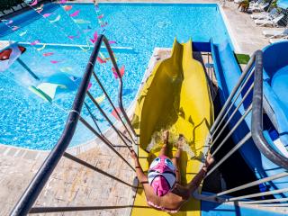 Child on yellow slide at pool with colorful decorations.