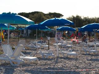 Beach with loungers and blue umbrellas on pebbles.