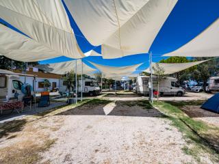 Campsite with RVs and tents under shade sails.