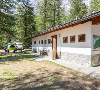 Edificio in campeggio tra gli alberi, con tenda e persone sedute.