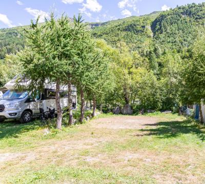 Campeggio tra le montagne con camper e tenda, circondato da alberi verdi.