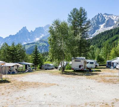 Campeggio montano con camper e roulotte, circondato da alberi e montagne innevate.