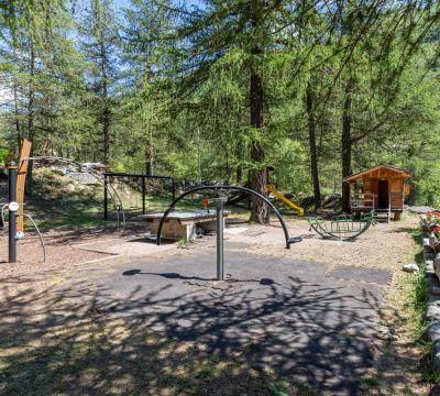 Parco giochi all'aperto tra gli alberi con attrezzature e casetta di legno.