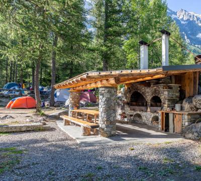 Area barbecue in campeggio montano con tende e vista sulle montagne.