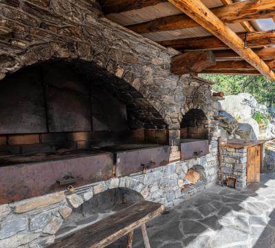 Forno in pietra all'aperto con tetto in legno, immerso nella natura.