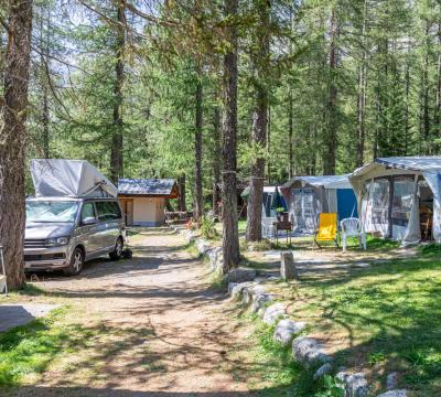 Campeggio tra gli alberi con tende, camper e sedie all'aperto.