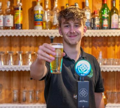 Giovane barista che serve una birra con un sorriso in un bar accogliente.