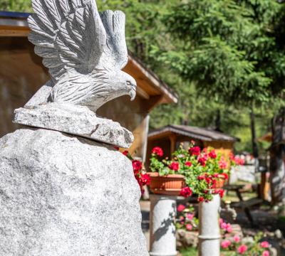 Statua d'aquila in pietra con fiori e alberi sullo sfondo.