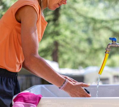 Persona lava i piatti all'aperto con acqua corrente.