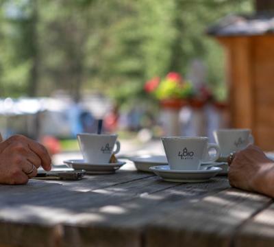 Due persone sorseggiano caffè all'aperto su un tavolo di legno.