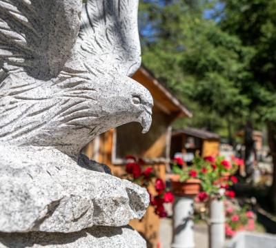 Statua di aquila in pietra con sfondo di fiori e casette di legno.