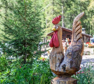 Scultura di gallo in legno in un giardino boscoso.