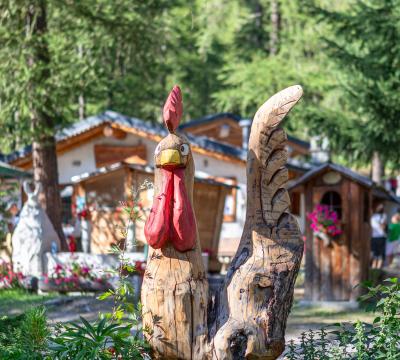 Scultura in legno di un gallo in un giardino fiorito.