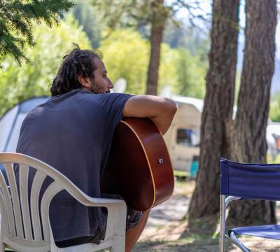 Uomo seduto all'aperto suona la chitarra in un campeggio.