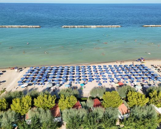 Spiaggia affollata con ombrelloni blu e mare calmo.