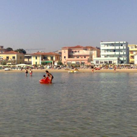 Crowded beach with colorful buildings in the background and people in the water.