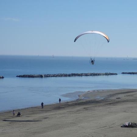 Paragliding over the beach with calm sea and clear sky.