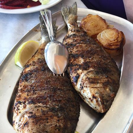 Grilled fish with lemon and roasted onions on a silver platter.