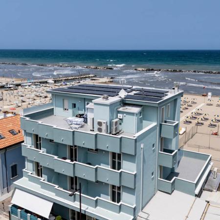 Modern seaside hotel, clear sky, and beach with umbrellas.